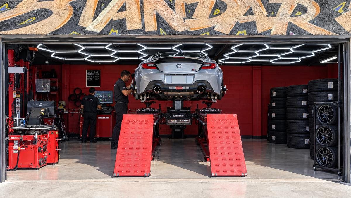 Technicians working under a lifted Toyota sports coupe in the red service bay at LA Standard in Sun Valley